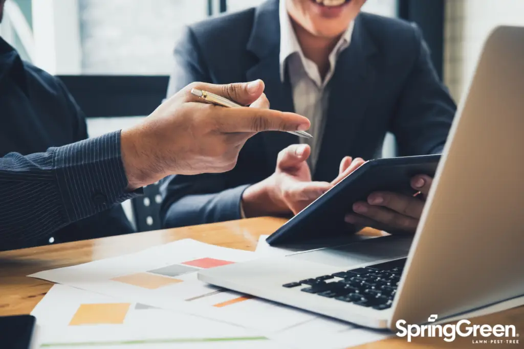 two men sitting at desk working pointing at laptop