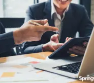 two men sitting at desk working pointing at laptop